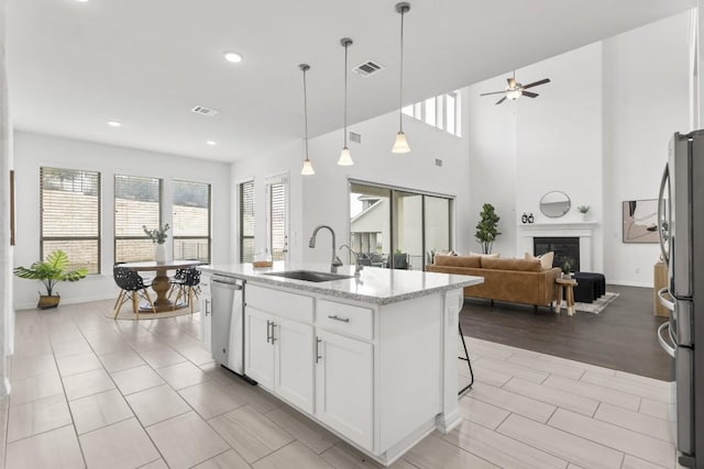 kitchen featuring sink, hanging light fixtures, stainless steel appliances, a center island with sink, and white cabinets