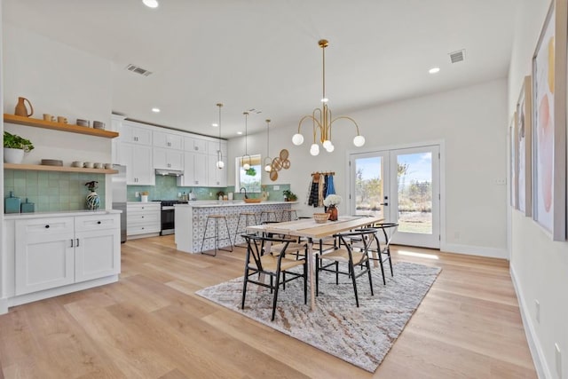 dining area with french doors, a notable chandelier, sink, and light wood-type flooring