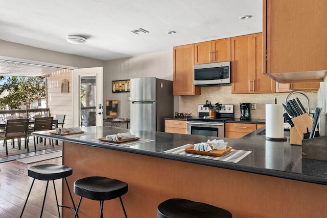 kitchen with a kitchen breakfast bar, backsplash, stainless steel appliances, and dark hardwood / wood-style floors