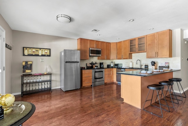 kitchen featuring sink, dark hardwood / wood-style flooring, a kitchen bar, kitchen peninsula, and stainless steel appliances