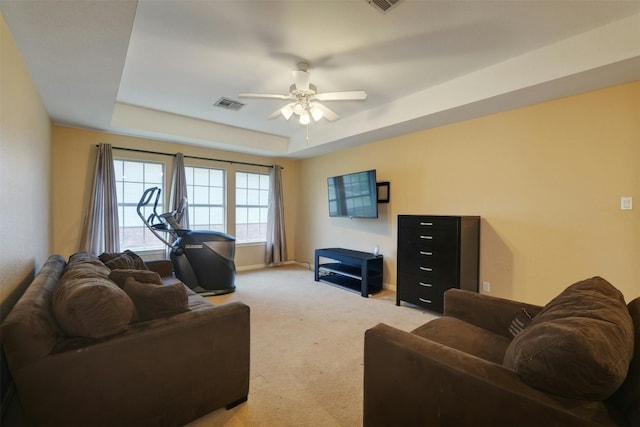 living room with a tray ceiling, ceiling fan, and light colored carpet