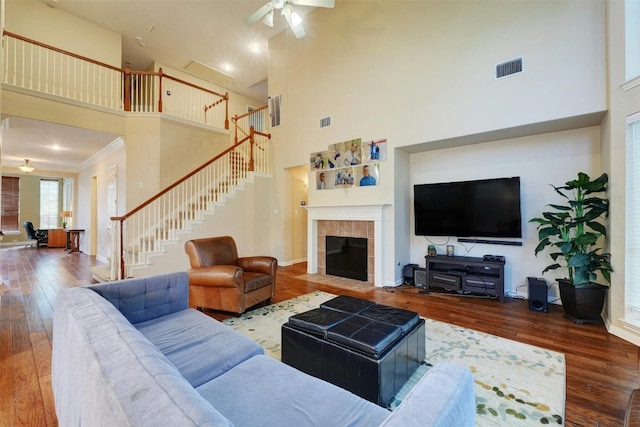 living room featuring a tiled fireplace, ceiling fan, a towering ceiling, and hardwood / wood-style flooring