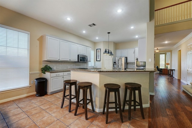 kitchen with white cabinetry, stainless steel appliances, dark stone counters, and tasteful backsplash