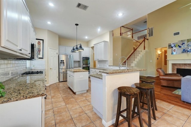 kitchen with white cabinets, decorative light fixtures, a kitchen island, and appliances with stainless steel finishes