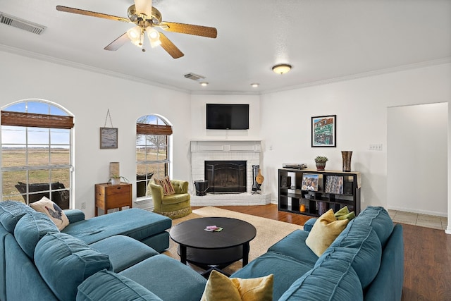 living room with hardwood / wood-style flooring, ceiling fan, crown molding, and a fireplace