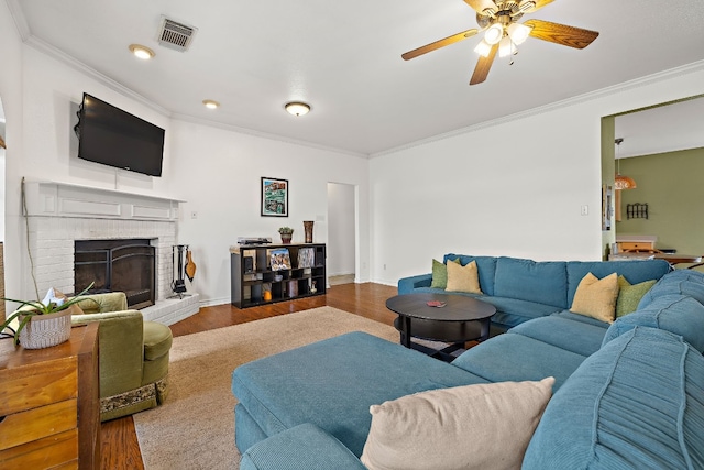 living room featuring ceiling fan, wood-type flooring, crown molding, and a brick fireplace