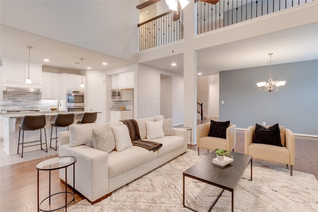 living room featuring light wood-type flooring, a high ceiling, and ceiling fan with notable chandelier