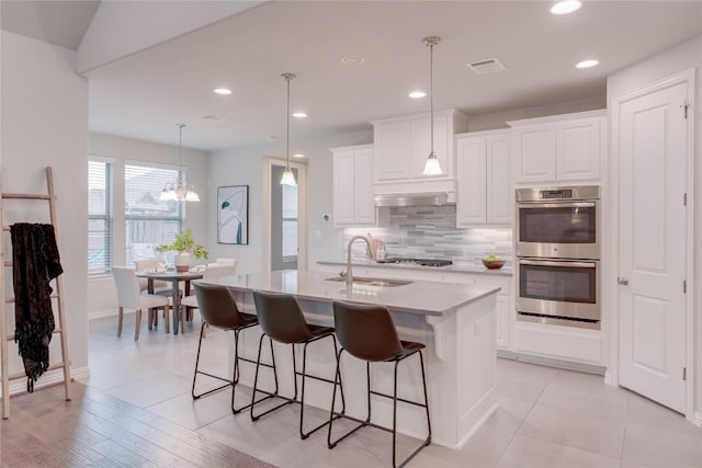 kitchen featuring decorative light fixtures, stainless steel appliances, white cabinetry, and a center island with sink