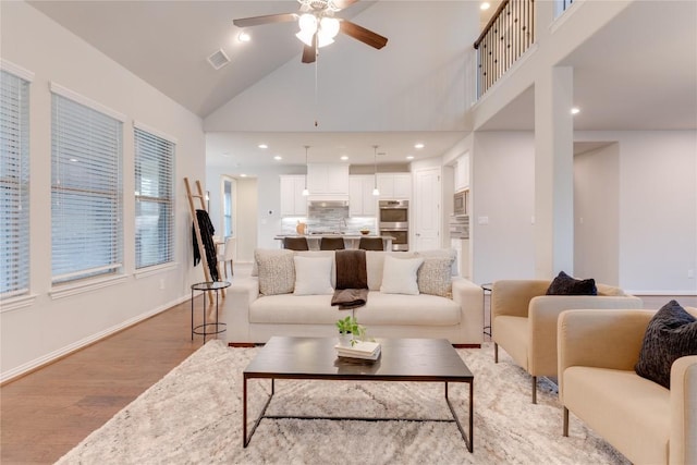 living room with ceiling fan, high vaulted ceiling, and light hardwood / wood-style floors