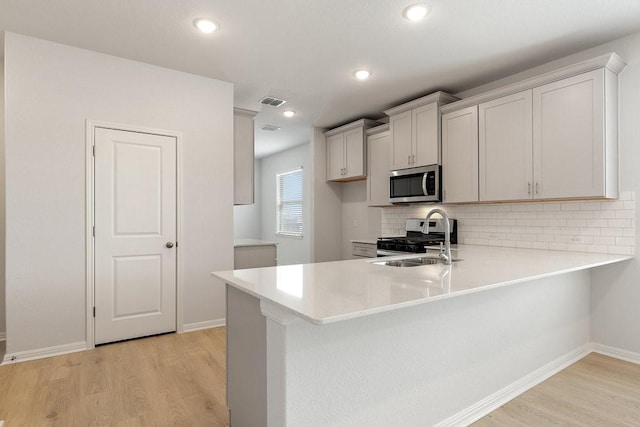 kitchen with stainless steel appliances, decorative backsplash, sink, kitchen peninsula, and light hardwood / wood-style flooring