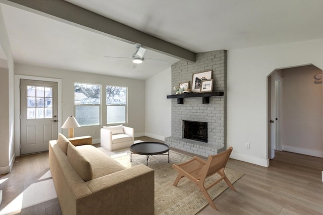 living room featuring vaulted ceiling with beams, ceiling fan, a fireplace, and light hardwood / wood-style floors