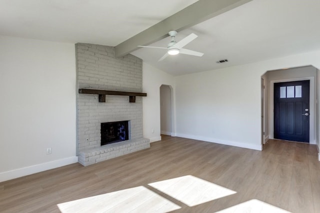 unfurnished living room with ceiling fan, lofted ceiling with beams, light wood-type flooring, and a brick fireplace