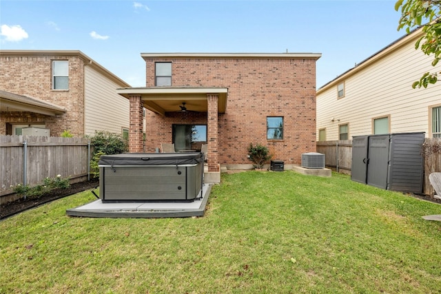 rear view of property with central air condition unit, a hot tub, a storage unit, and a lawn