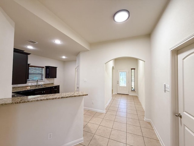 kitchen featuring kitchen peninsula, light stone countertops, sink, and light tile patterned floors