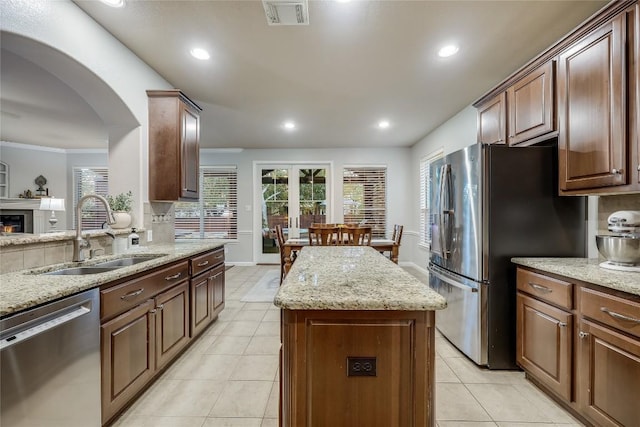 kitchen featuring light stone counters, a center island, stainless steel appliances, and sink