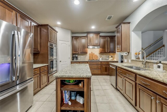 kitchen featuring light stone counters, stainless steel appliances, a kitchen island, and sink