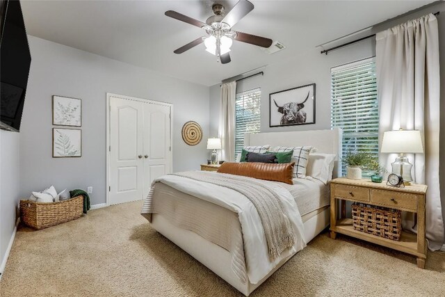 bedroom with multiple windows, ceiling fan, a closet, and light carpet