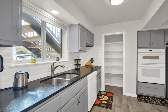 kitchen with tasteful backsplash, gray cabinetry, sink, and white appliances