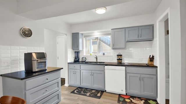 kitchen with sink, light hardwood / wood-style flooring, white dishwasher, gray cabinets, and decorative backsplash