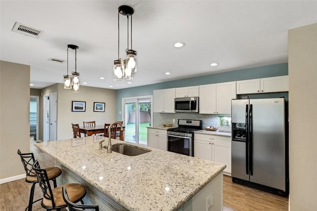 kitchen with appliances with stainless steel finishes, sink, pendant lighting, white cabinets, and an island with sink