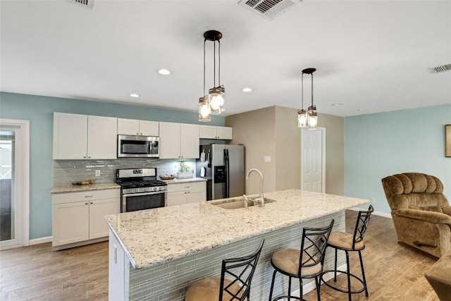 kitchen with sink, hanging light fixtures, stainless steel appliances, a center island with sink, and white cabinets