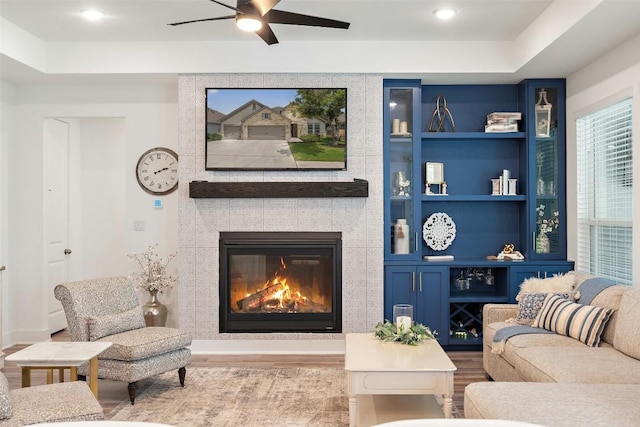 living room with a fireplace, built in shelves, light hardwood / wood-style floors, and ceiling fan