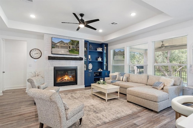 living room featuring hardwood / wood-style floors, built in features, a fireplace, and a tray ceiling