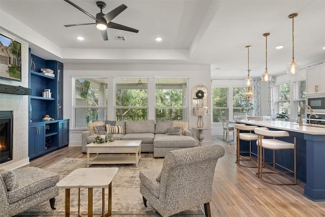 living room with built in shelves, ceiling fan, light wood-type flooring, a fireplace, and plenty of natural light