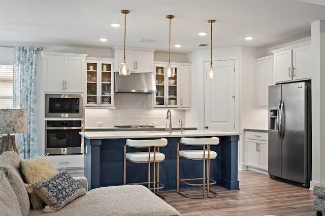 kitchen featuring hanging light fixtures, stainless steel appliances, exhaust hood, and an island with sink