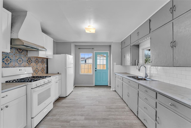 kitchen featuring white appliances, decorative backsplash, premium range hood, sink, and light hardwood / wood-style floors