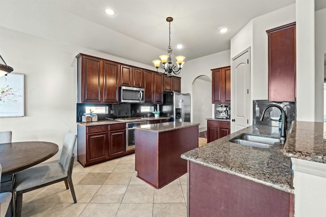 kitchen with sink, stainless steel appliances, dark stone counters, pendant lighting, and a kitchen island