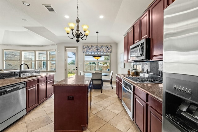 kitchen with pendant lighting, sink, a notable chandelier, a kitchen island, and stainless steel appliances