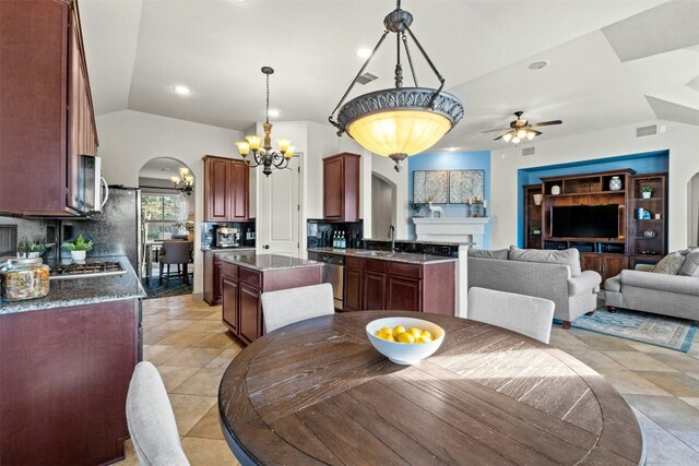 dining room featuring ceiling fan with notable chandelier, light tile patterned flooring, sink, and vaulted ceiling