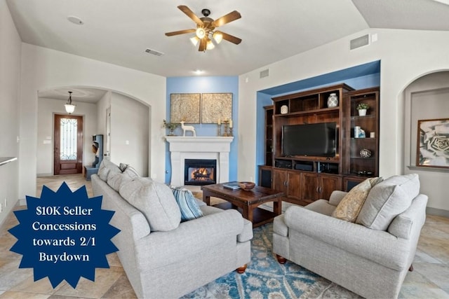 living area featuring vaulted ceiling, visible vents, arched walkways, and a glass covered fireplace