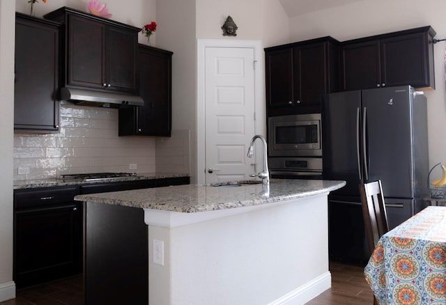 kitchen with a center island with sink, sink, light stone counters, dark hardwood / wood-style flooring, and stainless steel appliances