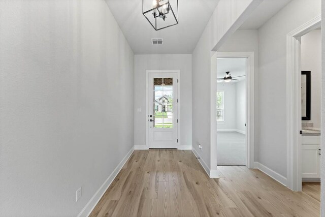 doorway with ceiling fan with notable chandelier and light wood-type flooring