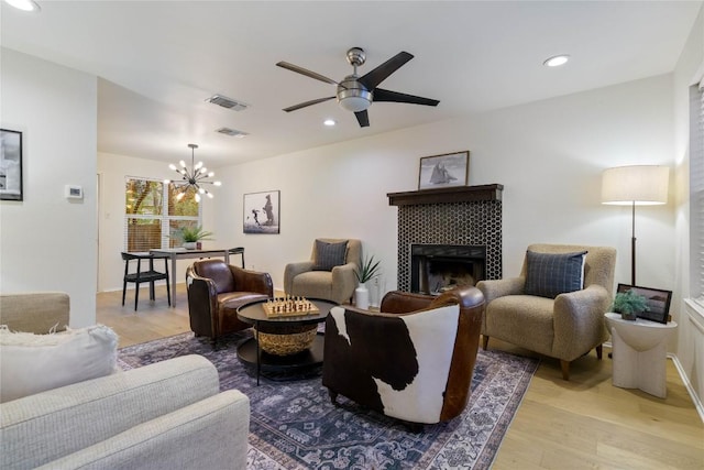 living room featuring ceiling fan with notable chandelier, light wood-type flooring, and a tiled fireplace