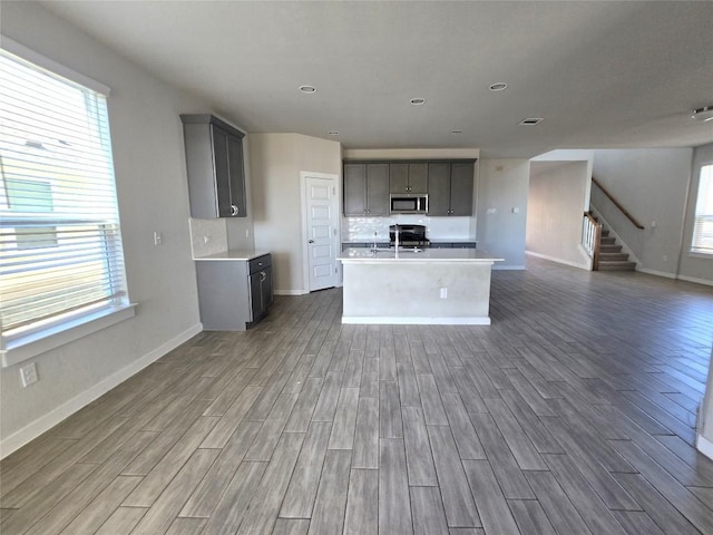 kitchen with decorative backsplash, gray cabinets, stainless steel appliances, and a center island with sink