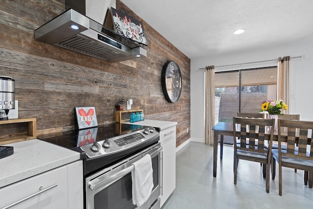 kitchen featuring stainless steel electric range, white cabinetry, wall chimney range hood, and wooden walls