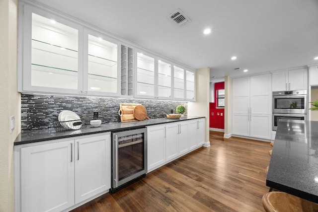 kitchen with dark hardwood / wood-style flooring, wine cooler, dark stone counters, stainless steel double oven, and white cabinetry