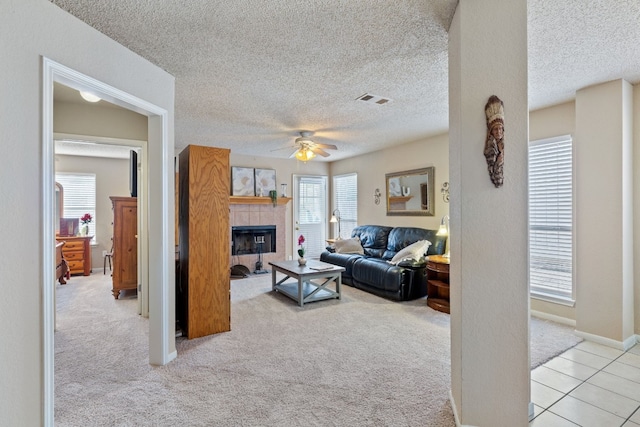 carpeted living room with a tile fireplace, a textured ceiling, plenty of natural light, and ceiling fan