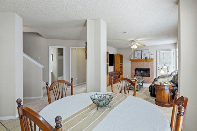 dining room with a textured ceiling, ceiling fan, light carpet, and a tile fireplace