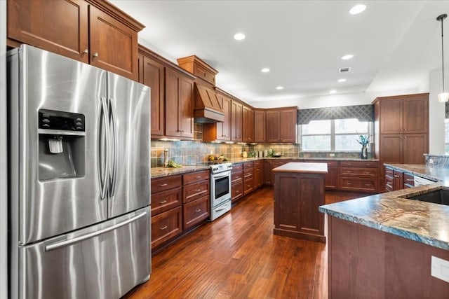 kitchen featuring premium range hood, dark stone counters, stainless steel appliances, pendant lighting, and dark hardwood / wood-style floors