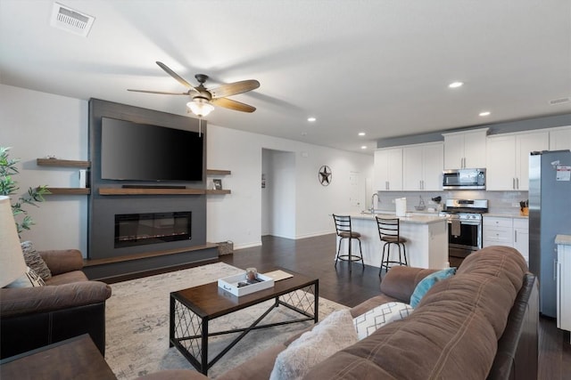 living room featuring ceiling fan, a large fireplace, dark hardwood / wood-style floors, and sink