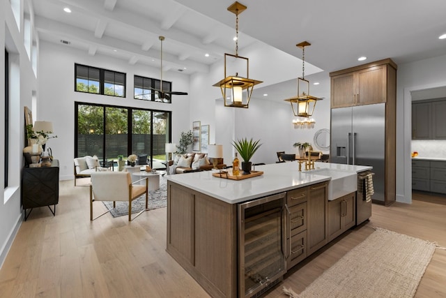 kitchen featuring wine cooler, a center island with sink, light hardwood / wood-style floors, and decorative light fixtures