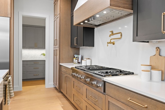 kitchen featuring tasteful backsplash, custom range hood, appliances with stainless steel finishes, and light hardwood / wood-style flooring