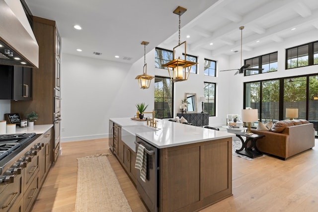 kitchen with beam ceiling, stainless steel appliances, pendant lighting, a kitchen island with sink, and custom exhaust hood