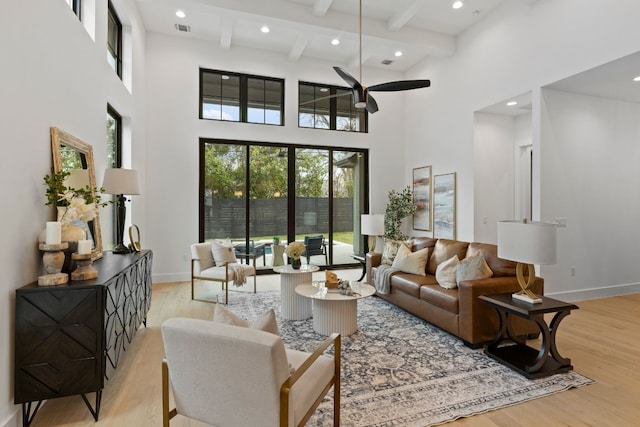 living room with beamed ceiling, a high ceiling, light hardwood / wood-style floors, and ceiling fan