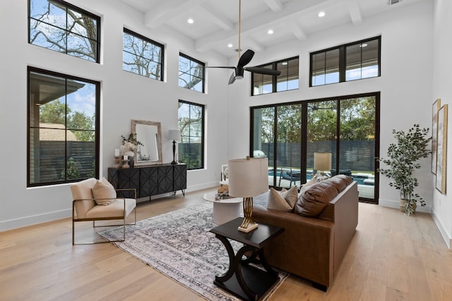 living room with beam ceiling, a high ceiling, and light wood-type flooring