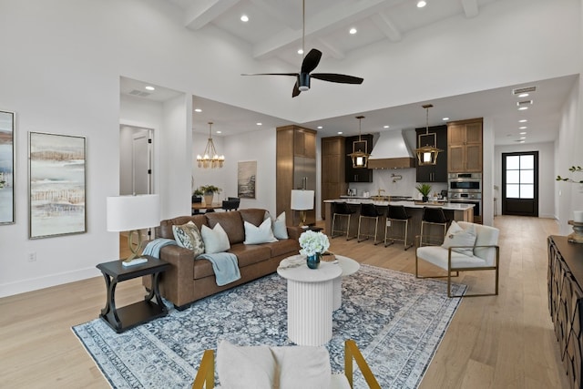 living room featuring a towering ceiling, light hardwood / wood-style flooring, beamed ceiling, and ceiling fan with notable chandelier